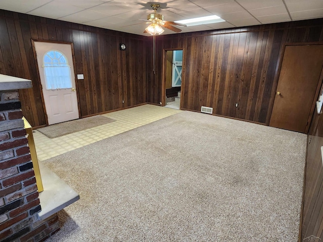 unfurnished living room with ceiling fan, a drop ceiling, carpet, and wood walls