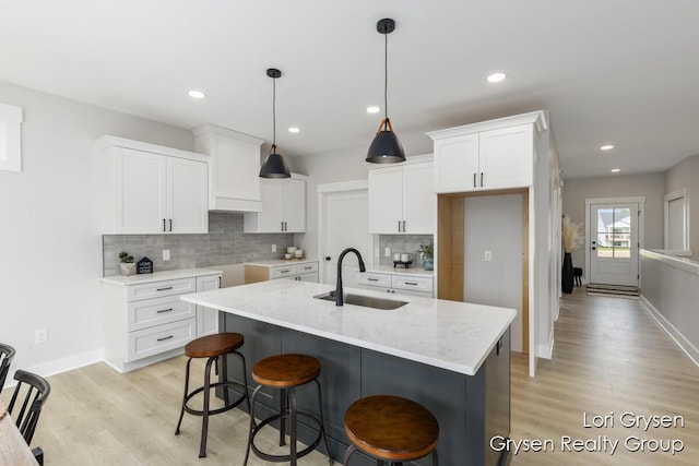 kitchen featuring a kitchen island with sink, tasteful backsplash, light wood-type flooring, a sink, and white cabinetry