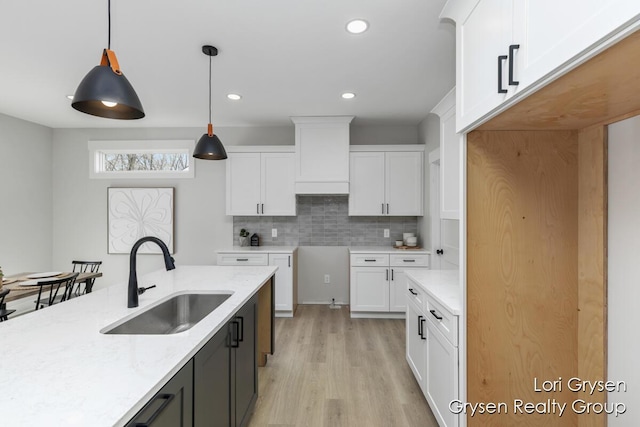 kitchen featuring pendant lighting, decorative backsplash, light wood-type flooring, white cabinets, and a sink