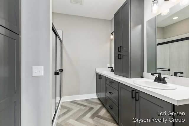 bathroom with a sink, baseboards, a shower stall, and double vanity