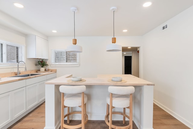 kitchen with sink, white cabinetry, hanging light fixtures, light hardwood / wood-style floors, and a kitchen island