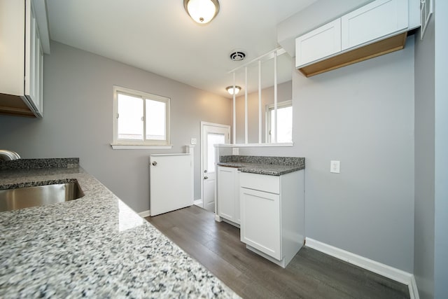 kitchen featuring sink, white cabinetry, dark hardwood / wood-style flooring, stone counters, and pendant lighting