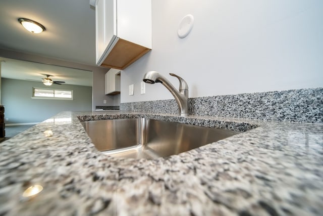 interior details with white cabinetry, sink, light stone countertops, and ceiling fan