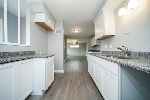 kitchen with sink, white cabinets, ceiling fan, light stone countertops, and light hardwood / wood-style flooring