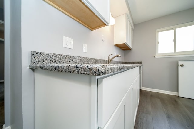 kitchen with white cabinetry, dark hardwood / wood-style flooring, sink, and dark stone countertops