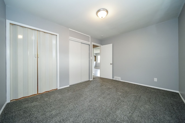 unfurnished bedroom featuring two closets and dark carpet