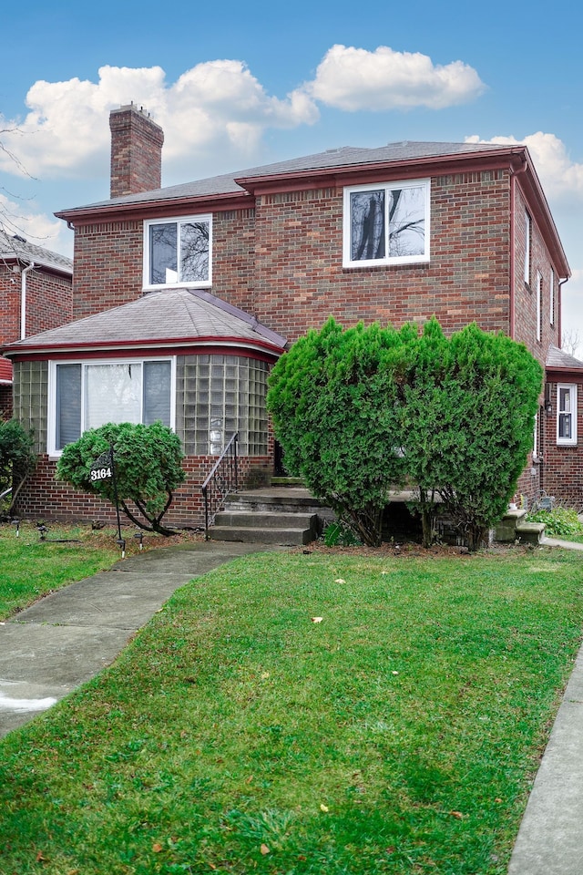 view of front facade with brick siding, a front lawn, and a chimney