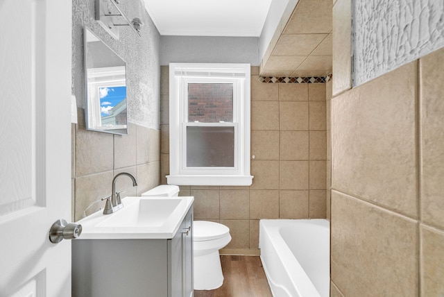 bathroom featuring tile walls, hardwood / wood-style flooring, vanity, toilet, and a bath