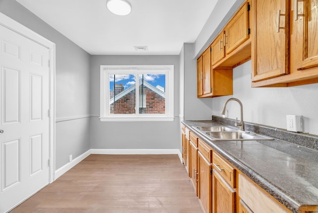 kitchen with dark stone counters, sink, and light hardwood / wood-style flooring