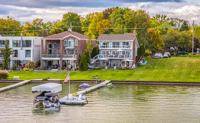 back of property with a water view, a balcony, and a lawn