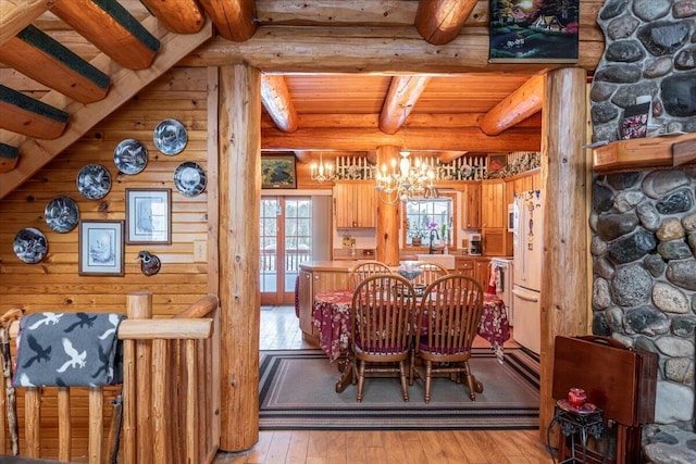 dining space with beamed ceiling, a notable chandelier, log walls, and light hardwood / wood-style floors