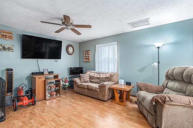 living room featuring hardwood / wood-style flooring, ceiling fan, and a textured ceiling