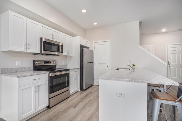 kitchen with light hardwood / wood-style flooring, a breakfast bar, white cabinetry, stainless steel appliances, and light stone countertops