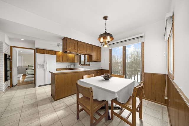 kitchen featuring a kitchen island, wood walls, white refrigerator with ice dispenser, double oven, and pendant lighting