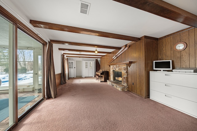 unfurnished living room featuring beamed ceiling, carpet flooring, a stone fireplace, and wooden walls