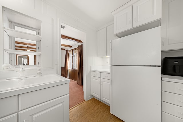 kitchen featuring light hardwood / wood-style flooring, sink, white refrigerator, crown molding, and white cabinets