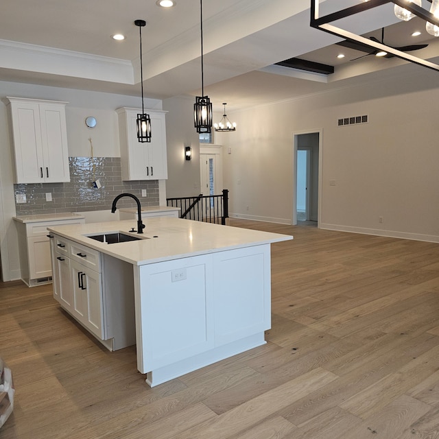 kitchen featuring sink, white cabinetry, a raised ceiling, hanging light fixtures, and a kitchen island with sink