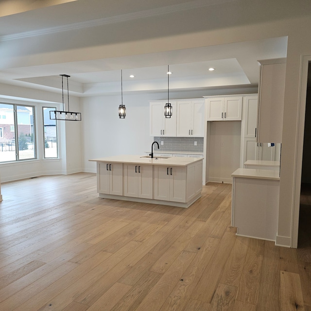 kitchen featuring a center island with sink, light hardwood / wood-style flooring, hanging light fixtures, a tray ceiling, and sink