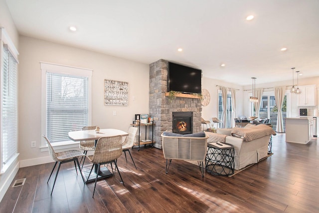 living room featuring a stone fireplace, dark hardwood / wood-style floors, and a wealth of natural light