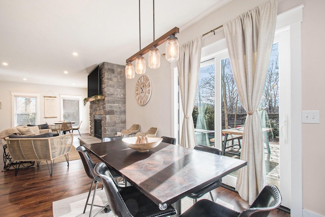 dining area with dark wood-type flooring and a stone fireplace