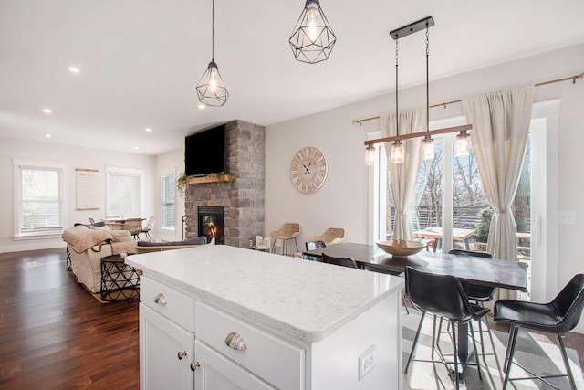 kitchen featuring a kitchen island, a stone fireplace, pendant lighting, white cabinets, and dark hardwood / wood-style flooring