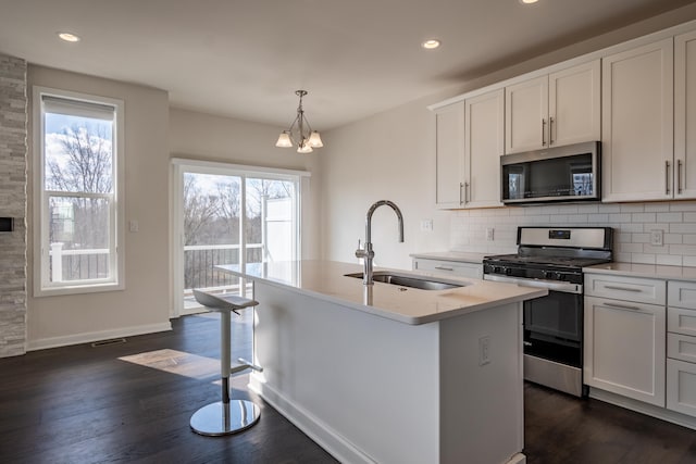 kitchen featuring appliances with stainless steel finishes, dark wood-type flooring, a sink, and decorative backsplash