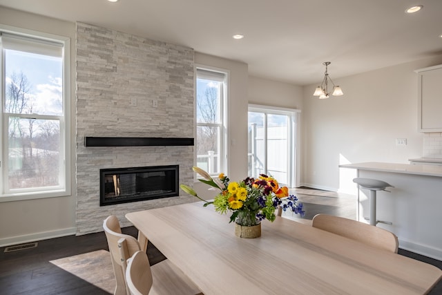 dining room with dark wood-style flooring, recessed lighting, visible vents, a stone fireplace, and baseboards