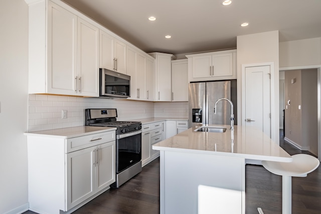 kitchen featuring dark wood finished floors, a sink, stainless steel appliances, white cabinetry, and backsplash