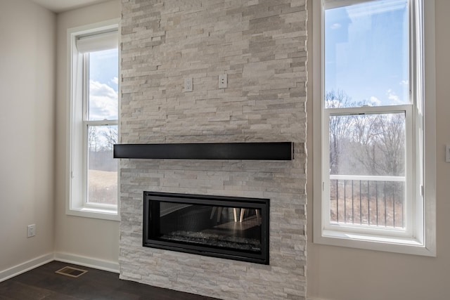 room details featuring visible vents, a fireplace, baseboards, and wood finished floors