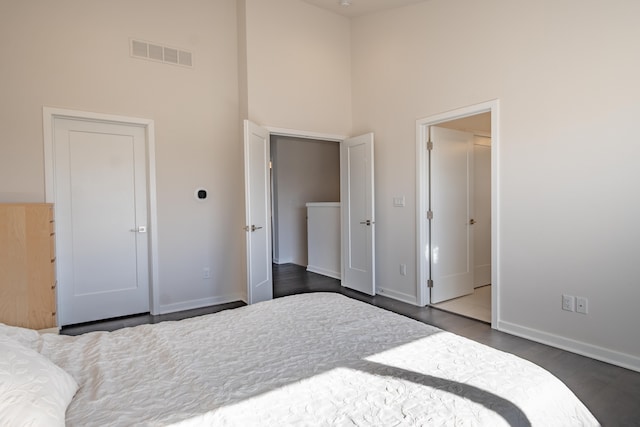 bedroom with a high ceiling, dark wood finished floors, visible vents, and baseboards