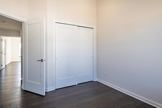 unfurnished bedroom with a closet, dark wood-style flooring, and baseboards