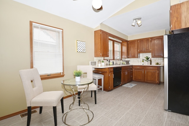 kitchen featuring sink, backsplash, black dishwasher, ceiling fan, and stainless steel fridge