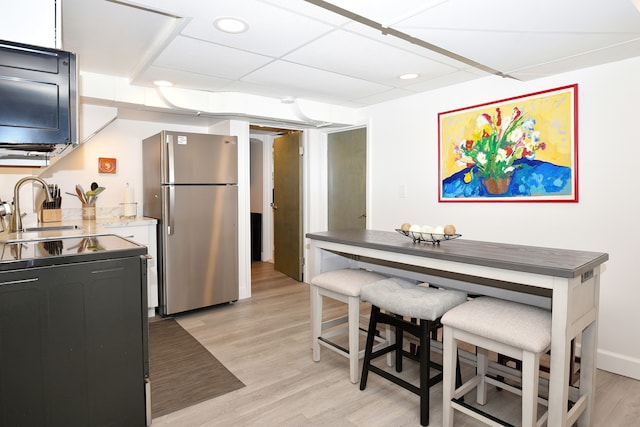 kitchen with a paneled ceiling, electric stove, light wood-type flooring, stainless steel refrigerator, and sink