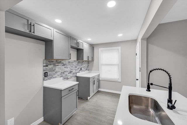 kitchen with tasteful backsplash, gray cabinets, sink, and light wood-type flooring