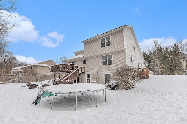 snow covered back of property featuring a wooden deck and a trampoline