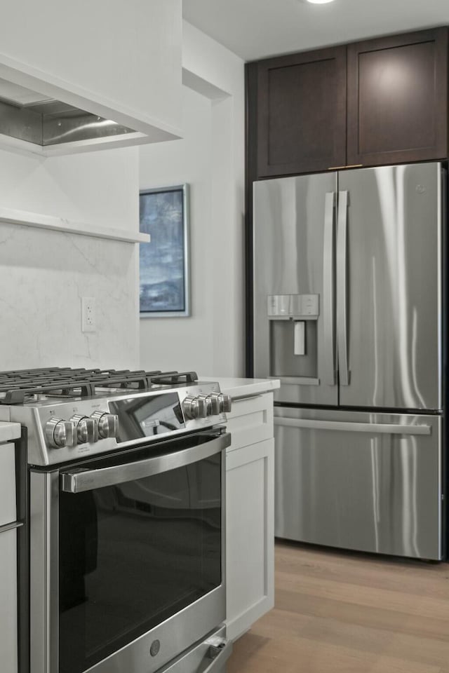 kitchen featuring stainless steel appliances, dark brown cabinetry, tasteful backsplash, white cabinets, and light wood-type flooring