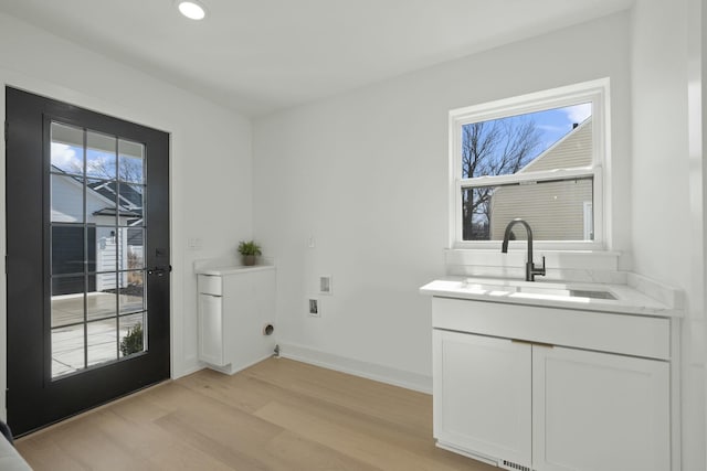 clothes washing area with cabinets, sink, washer hookup, and light wood-type flooring