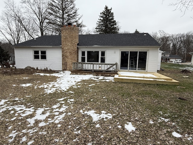 snow covered house with roof with shingles, a chimney, and a wooden deck