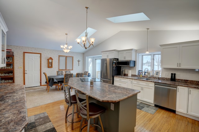 kitchen with white cabinetry, decorative light fixtures, sink, appliances with stainless steel finishes, and a breakfast bar area