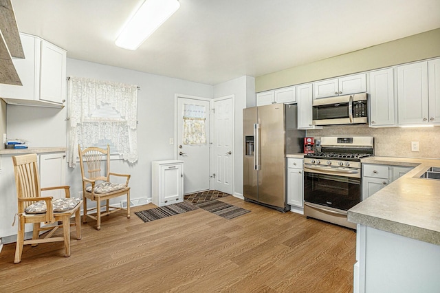 kitchen with tasteful backsplash, white cabinetry, appliances with stainless steel finishes, and light hardwood / wood-style floors