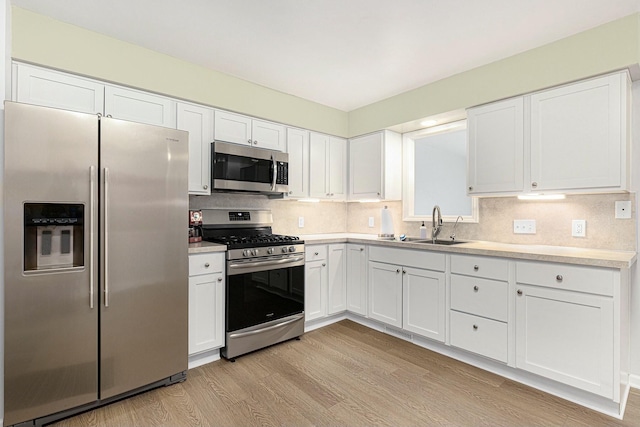 kitchen with sink, white cabinets, decorative backsplash, stainless steel appliances, and light hardwood / wood-style flooring