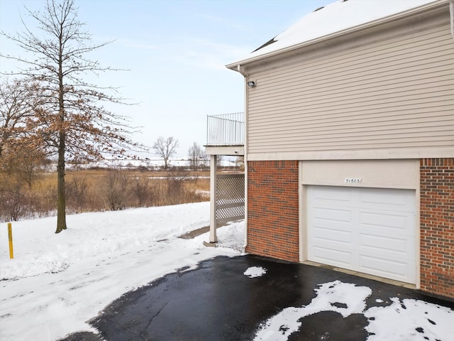 view of snow covered exterior featuring a garage, brick siding, and a balcony