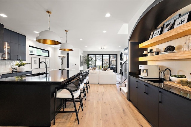 kitchen featuring a breakfast bar, decorative light fixtures, dark countertops, a sink, and dark cabinets