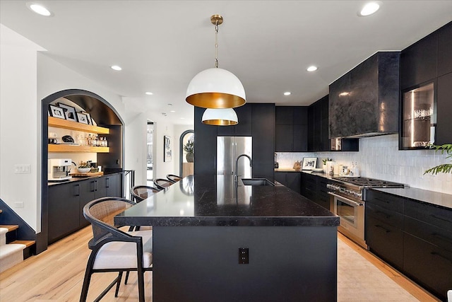 kitchen with a center island with sink, a breakfast bar area, stainless steel appliances, dark countertops, and a sink