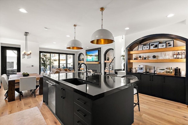 kitchen featuring dark countertops, hanging light fixtures, a sink, an island with sink, and dark cabinetry