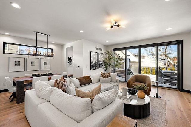 living area featuring baseboards, visible vents, light wood-style flooring, a notable chandelier, and recessed lighting