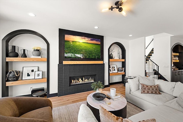 living area with built in features, recessed lighting, wood finished floors, a lit fireplace, and stairs