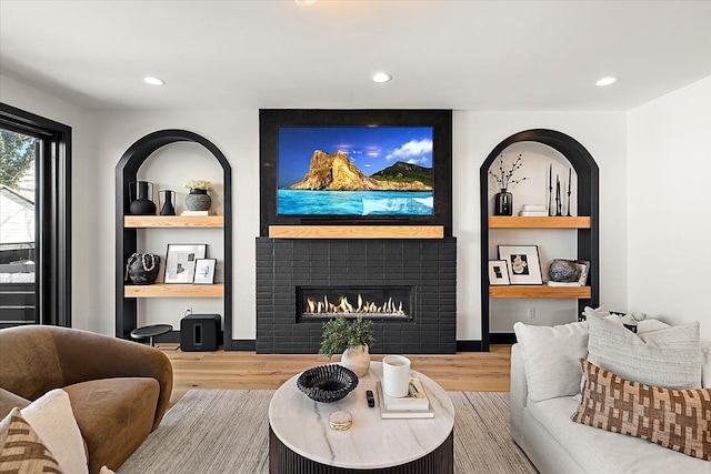 living area with built in shelves, a glass covered fireplace, recessed lighting, and wood finished floors