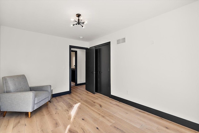 living area with a chandelier, light wood finished floors, visible vents, and baseboards