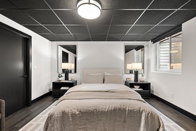 bedroom featuring a paneled ceiling, baseboards, and dark wood finished floors